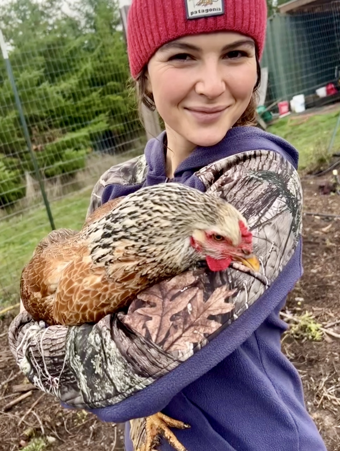 Mollie Ryerse smiling while holding one of her chickens in a garden